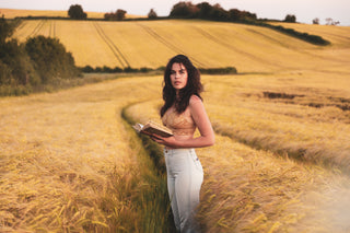Woman standing facing camera in a field wearing a golden coloured Honey bralette made of sustainable lace.