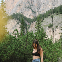 Woman standing in a mountainous area with rocky cliffs and greenery wearing a black Aberdevine underwired bra and jeans.