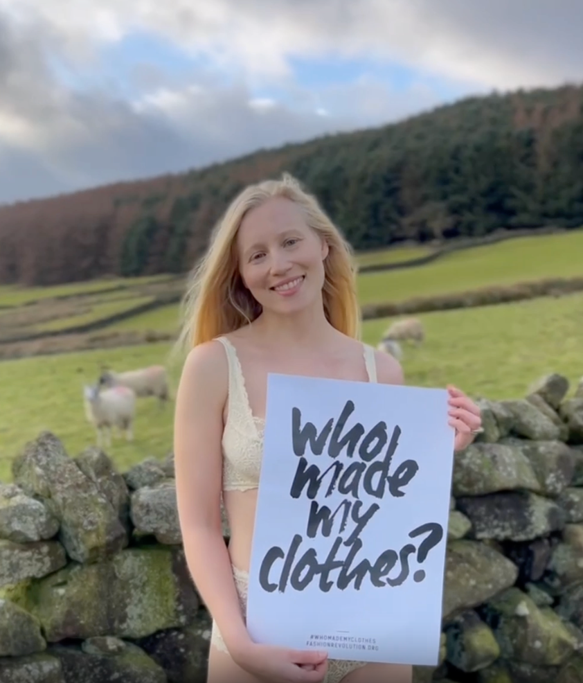 Video of a woman wearing cream lingerie and wellies in the Yorkshire Dales. She is holding a sign that reads "who made my clothes".