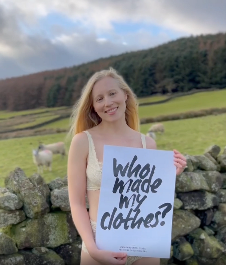 Video of a woman wearing cream lingerie and wellies in the Yorkshire Dales. She is holding a sign that reads "who made my clothes".