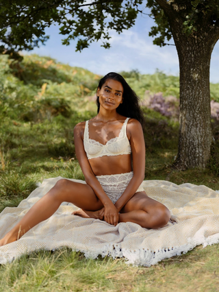 Model in the cream, lacy, Aberdevine underwired bra and matching high waisted knickers sat on a blanket in nature